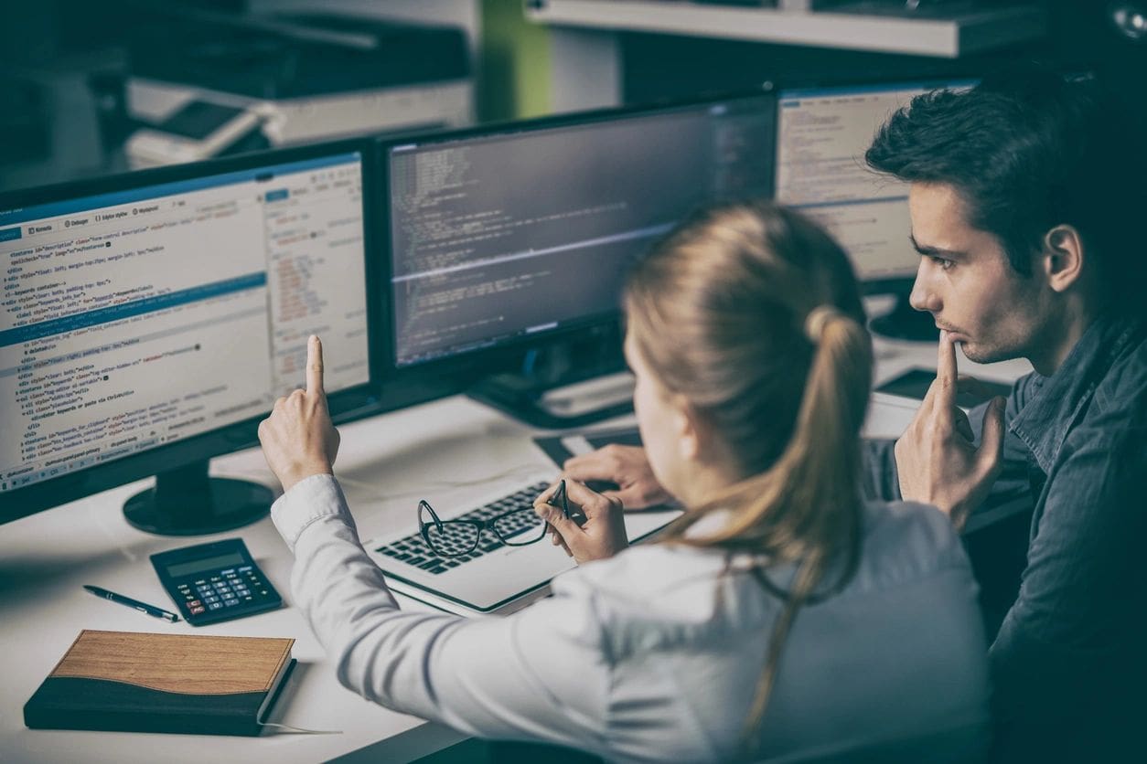 Two people sitting at a desk with computers.