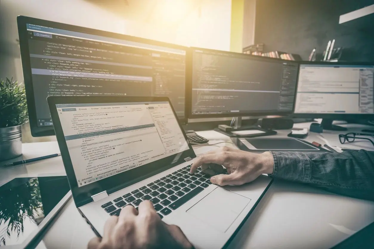 A person is using a laptop in front of multiple computers.