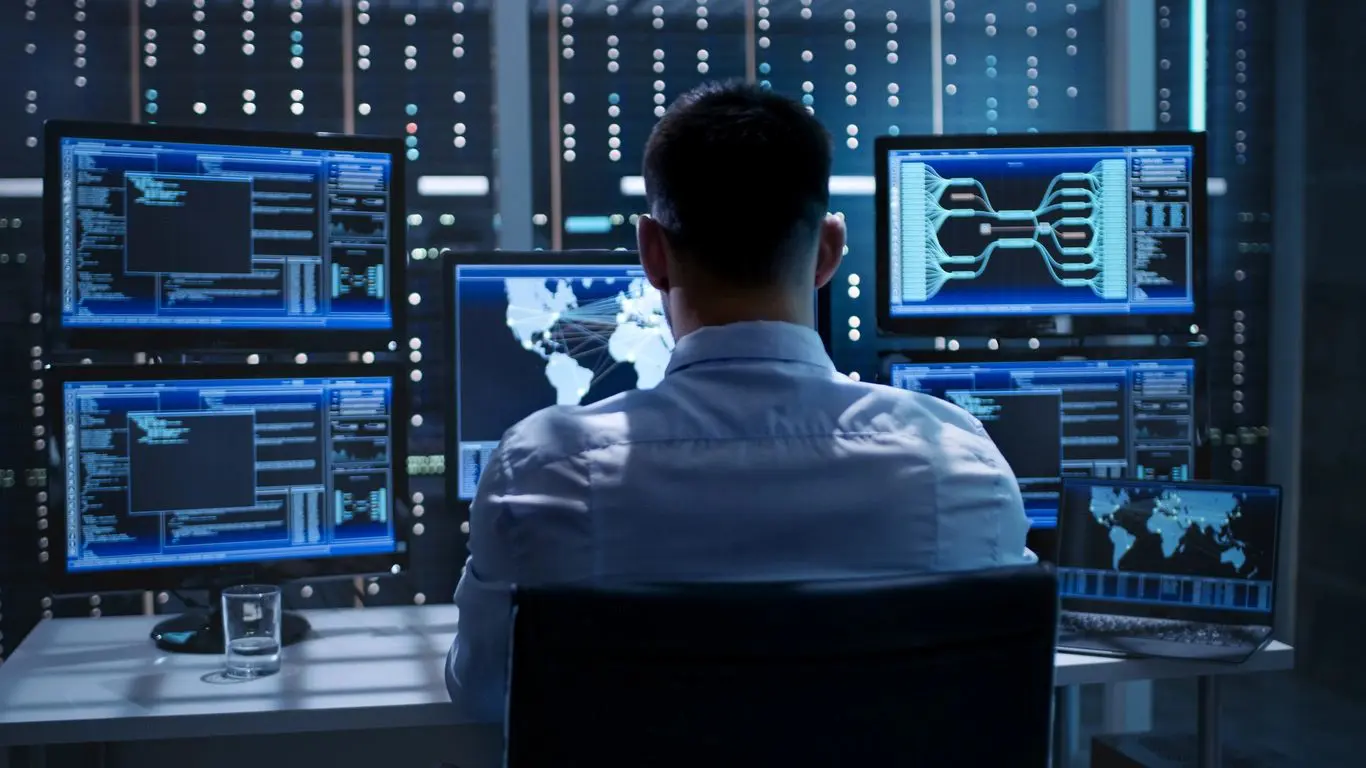 A man sitting in front of multiple computer screens.