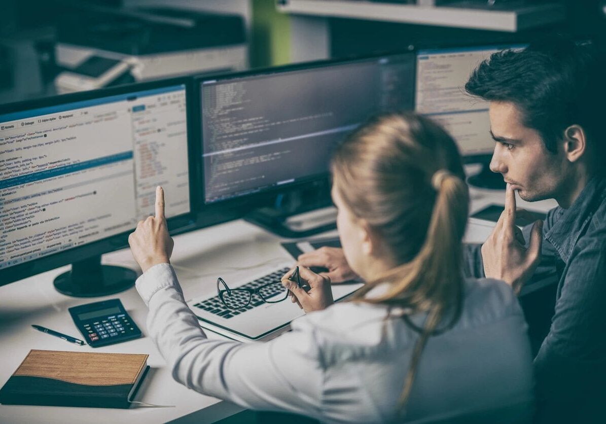 Two people sitting at a desk with computers.